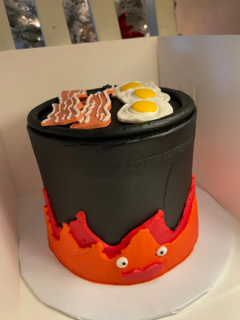Black frying-pan cake with a friendly fire character, bacon and eggs