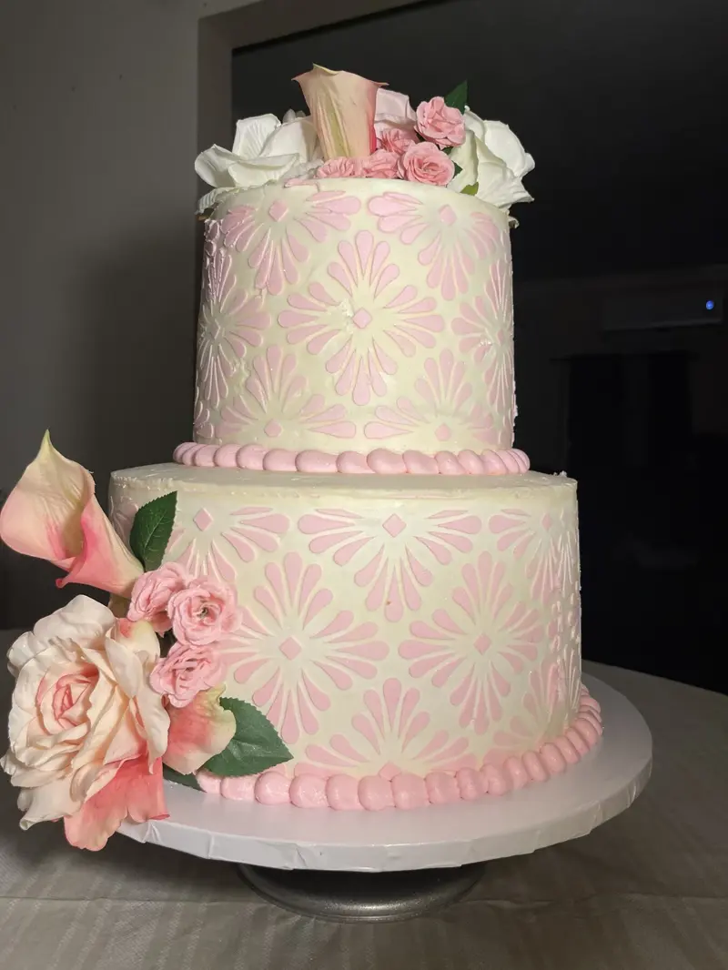 Two-tier ivory cake with a pink stencil pattern, roses and calla lilies