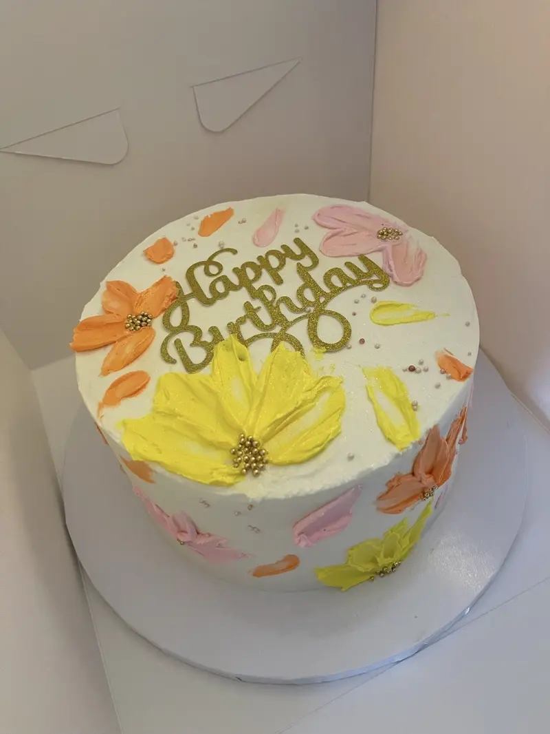 White cake with colorful piped flowers and a gold Happy Birthday topper