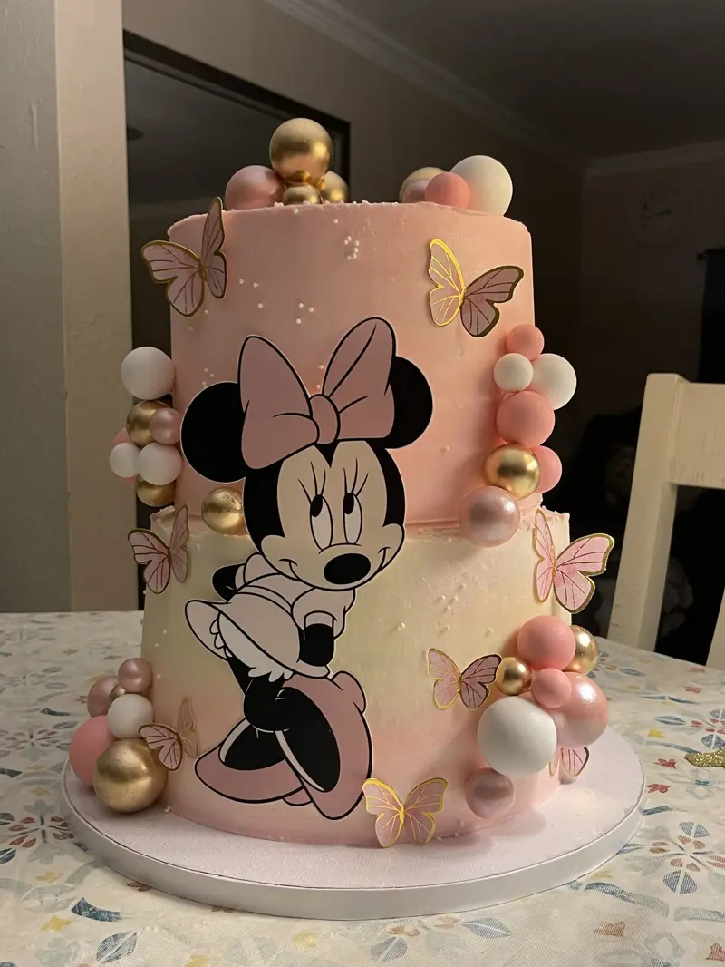 Two-tier pink Minnie Mouse cake with butterflies and gold spheres