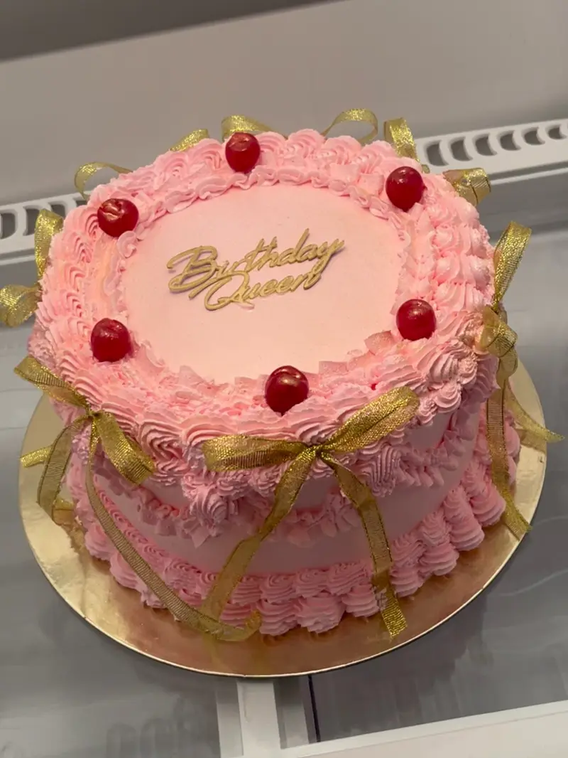 Pink vintage cake with cherries, gold ribbon and a Birthday Queen topper