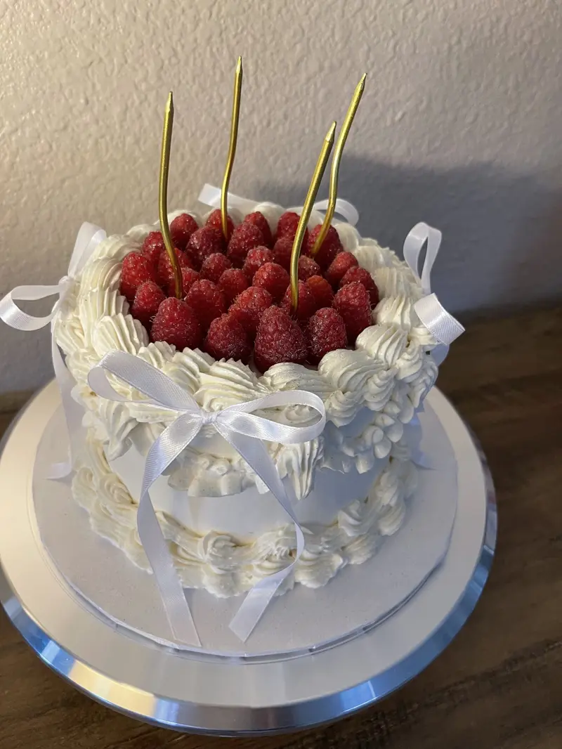 White vintage cake with piped ruffles, ribbon bows, fresh raspberries and gold candles