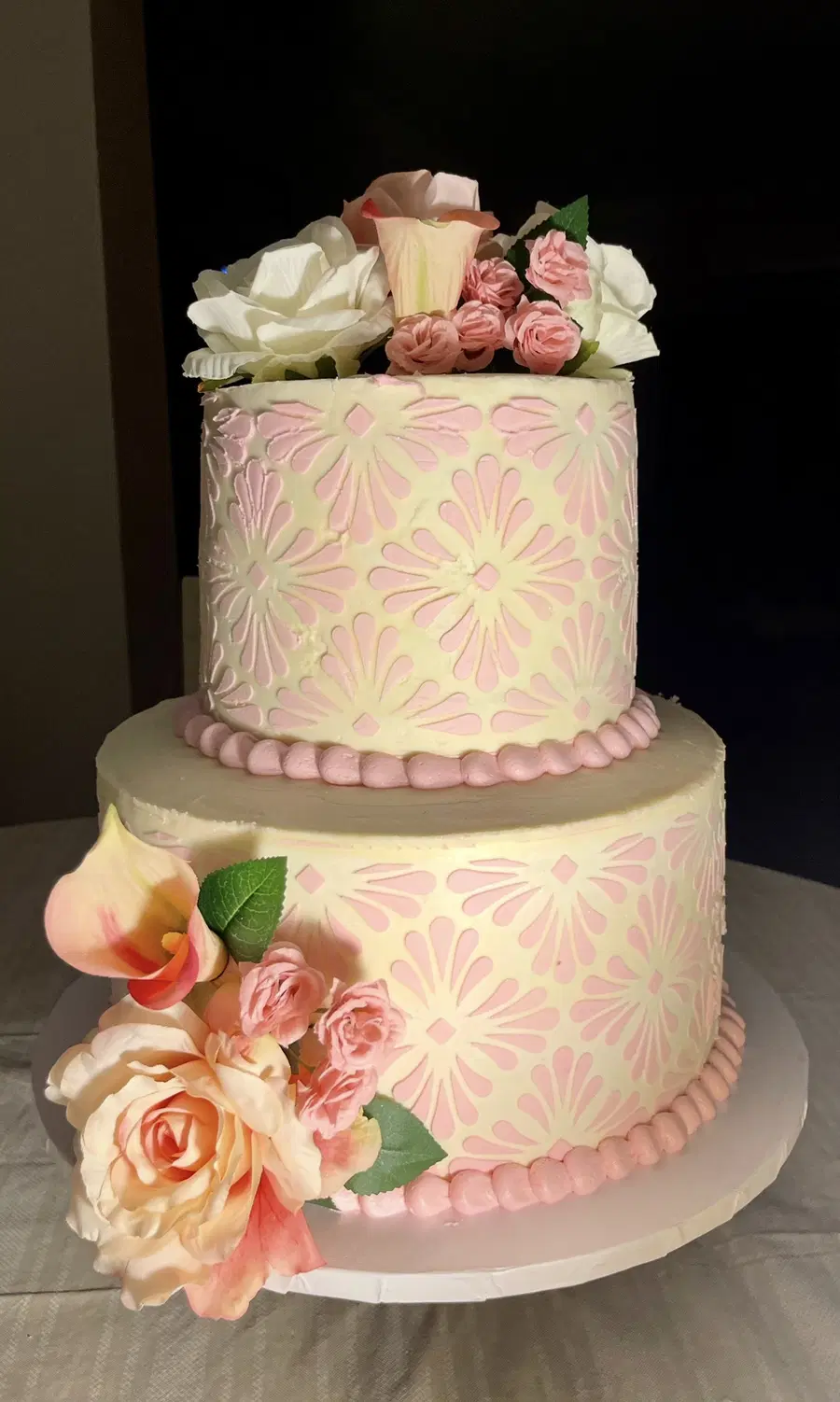 Two-tier ivory cake with a pink stencil pattern, roses and calla lilies